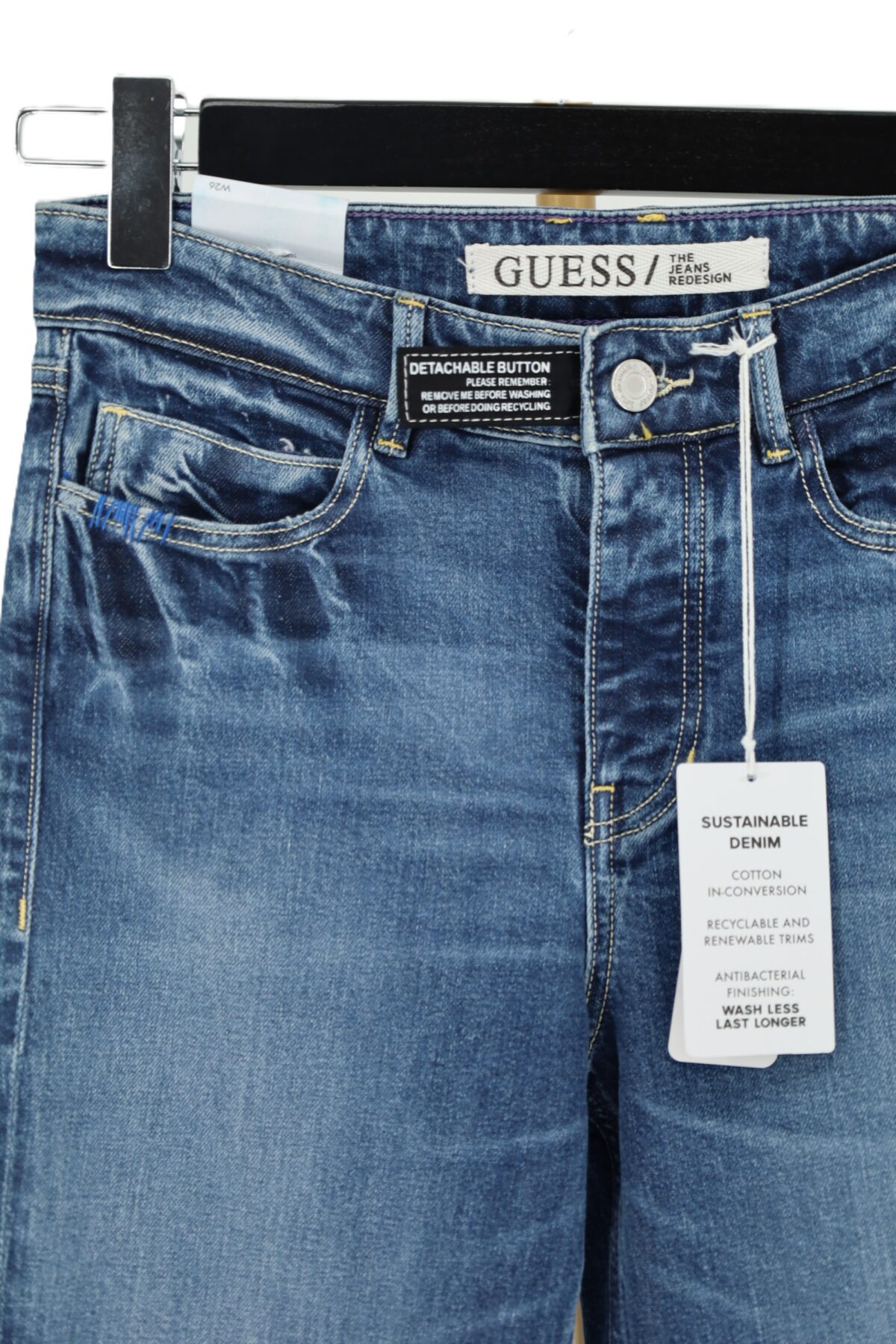 Zbliżenie na wysoki stan jeansów GUESS z naszywką Detachable Button i kodem modelu.