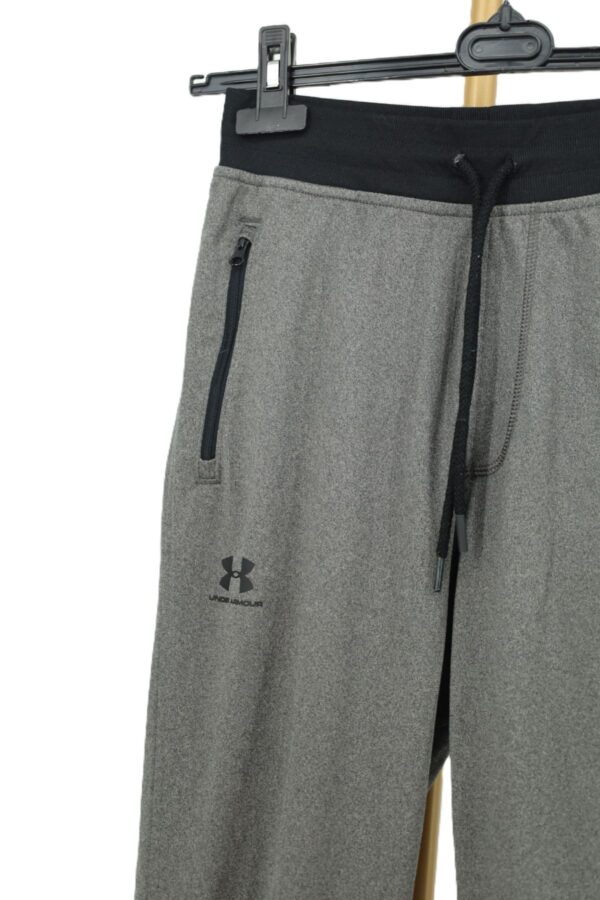 Zbliżenie na czarny zamek kieszeni bocznej i logo Under Armour na udzie.