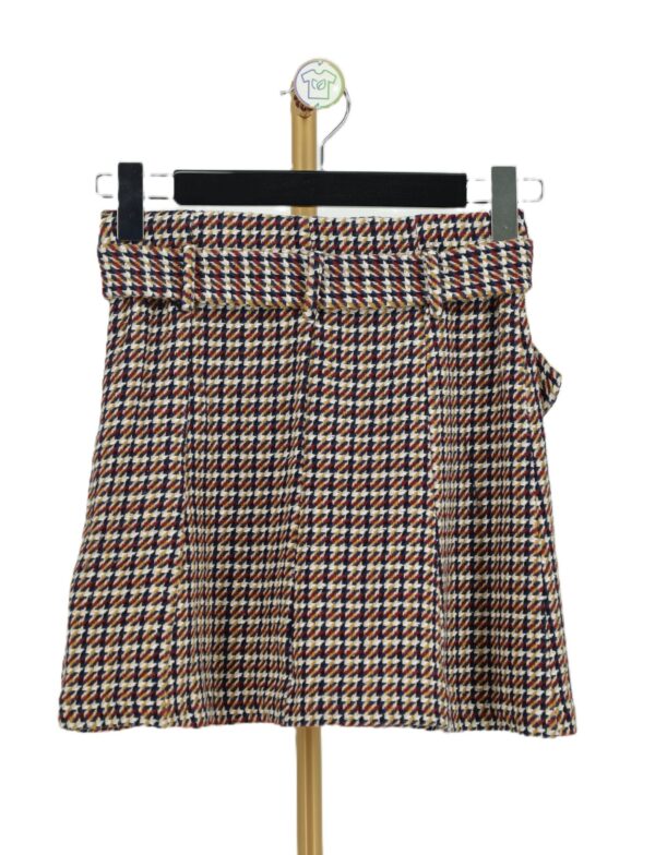 Tył trapezowej spódnicy mini w pepitkę houndstooth na wieszaku.